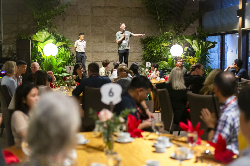 Conference delegates seated at round tables at an evening dinner while a speaker addresses the room