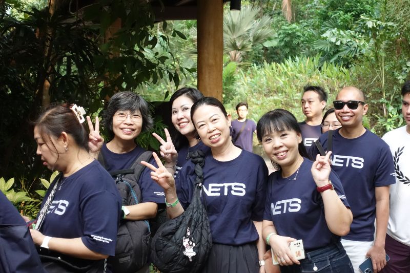NETS colleagues in matching navy T-shirts smile and make peace signs at Singapore Zoo